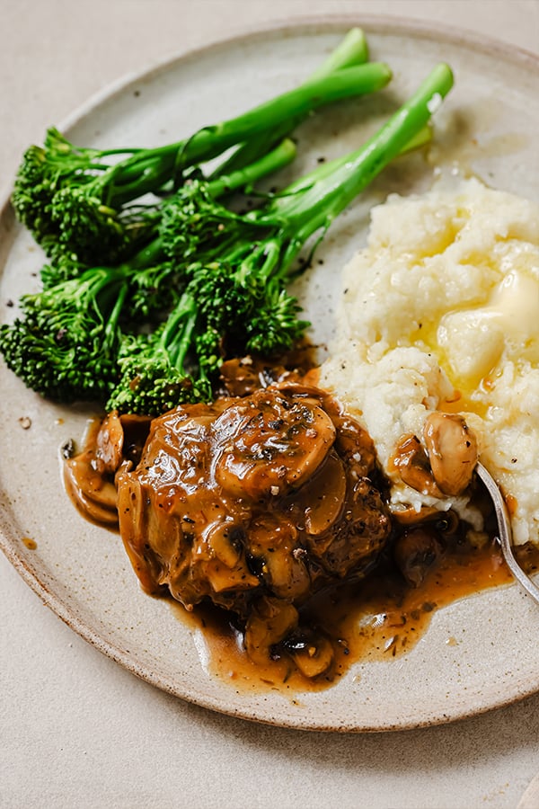 hamburger steak plated with a side of mashed cauliflower and broccolini.