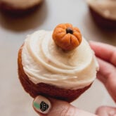 Person holding a pumpkin spice cupcake topped with a decorative pumpkin.