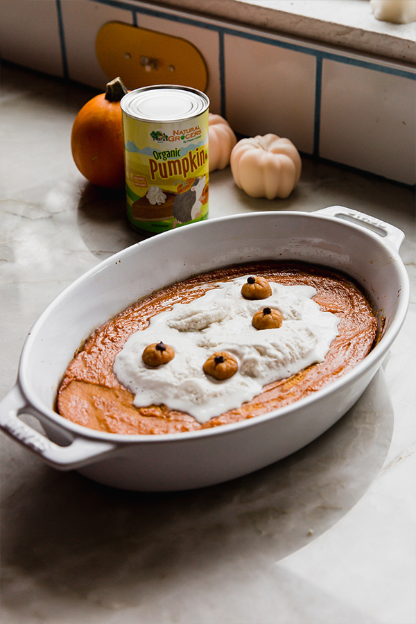 A finished baked pumpkin pudding sitting on the counter with canned pumpkin and mini pumpkins in the background.