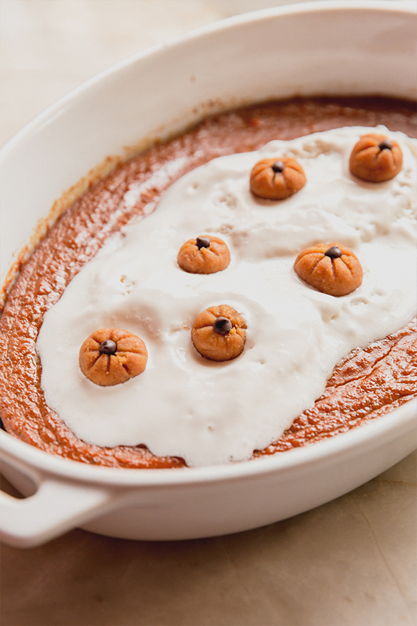 A serving bowl of baked pumpkin pudding with pumpkin buckeyes on top.