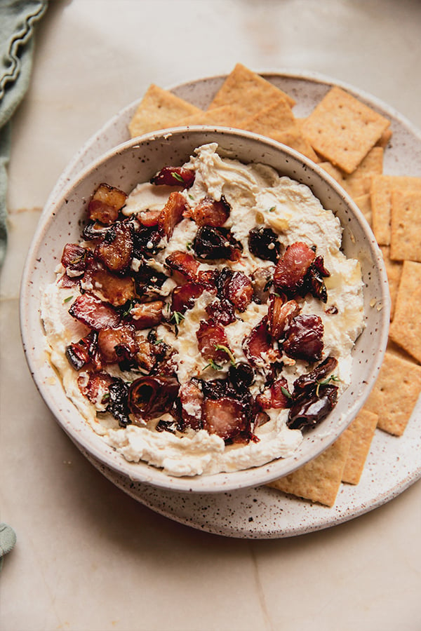 A bowl of bacon date dip with crackers ready for being enjoyed.
