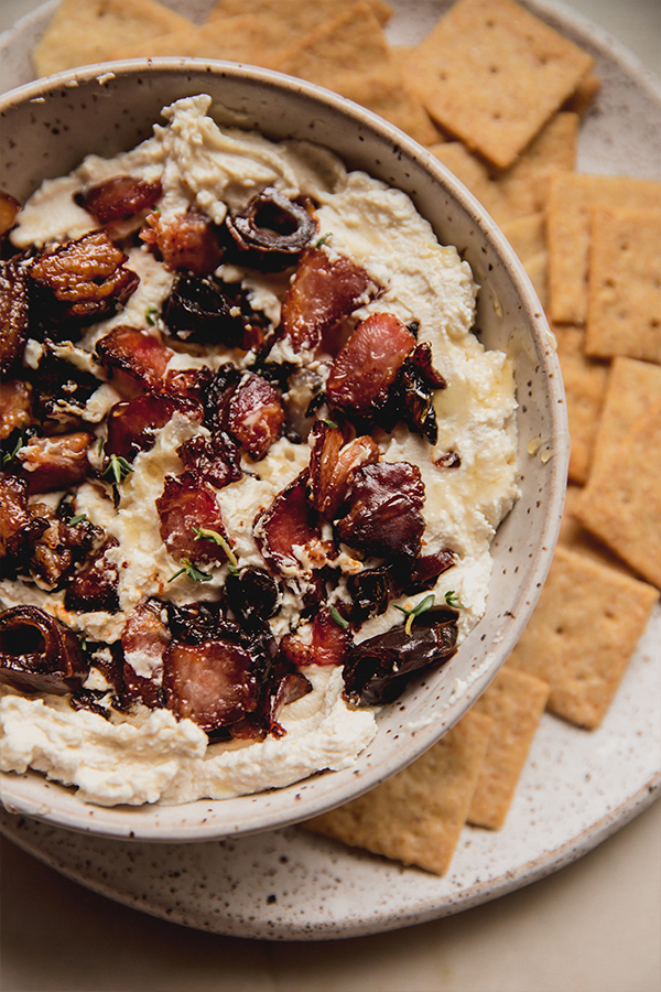 A serving bowl of bacon date dip with crackers surrounding it.