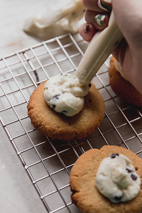 The cookies being topped with cannoli cream.