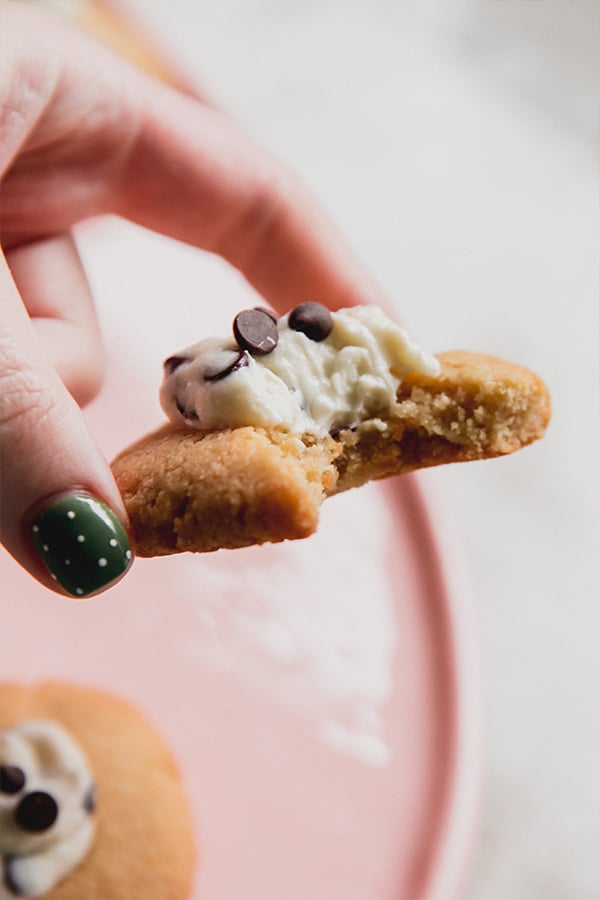 A cannoli thumbprint cookies being held in a hand with a bite taken out of it.