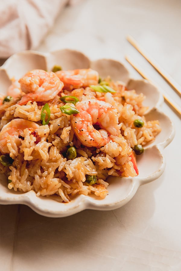 A bowl filled with sheet pan shrimp fried rice and chopsticks ready to be enjoyed.