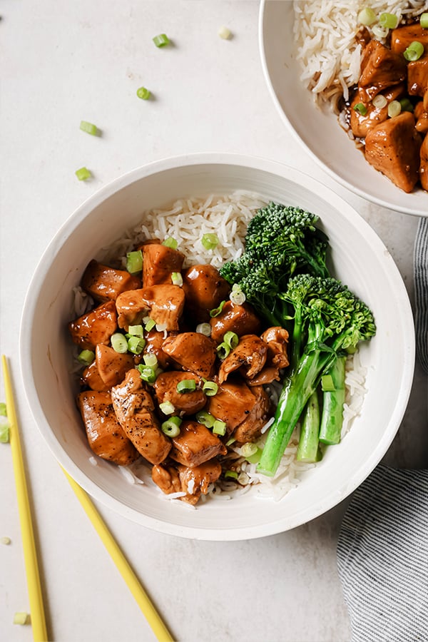 A bowl with bourbon chicken served with broccolini and rice noodles.
