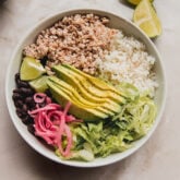 Bowl filled with chicken burrito bowl toppings such as avocado and beans.