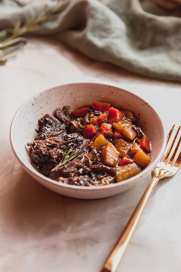 A bowl full of apple cider braised pot roast with vegetables.