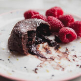 Partially-eaten lava cake on a plate with raspberries.