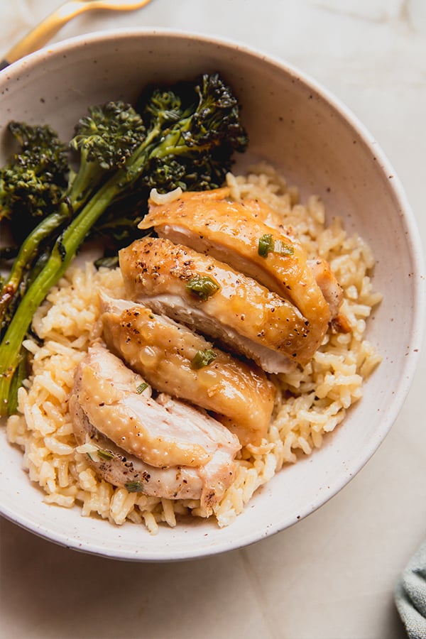 A bowl of rice cooker chicken, rice, and roasted broccolini.