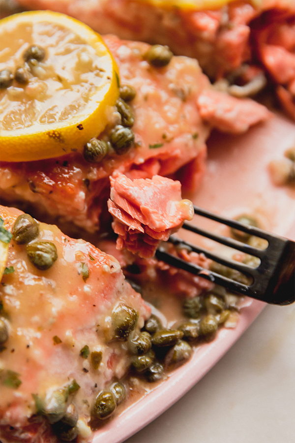 A fork taking a bite of salmon piccata off the serving platter.