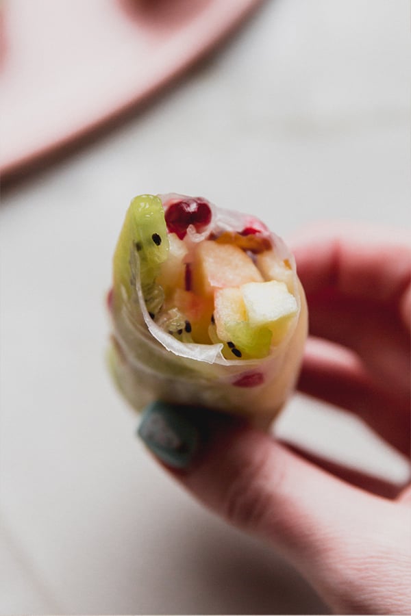 A fruit rice paper rolls with a bite taken out of it so you can see the center.