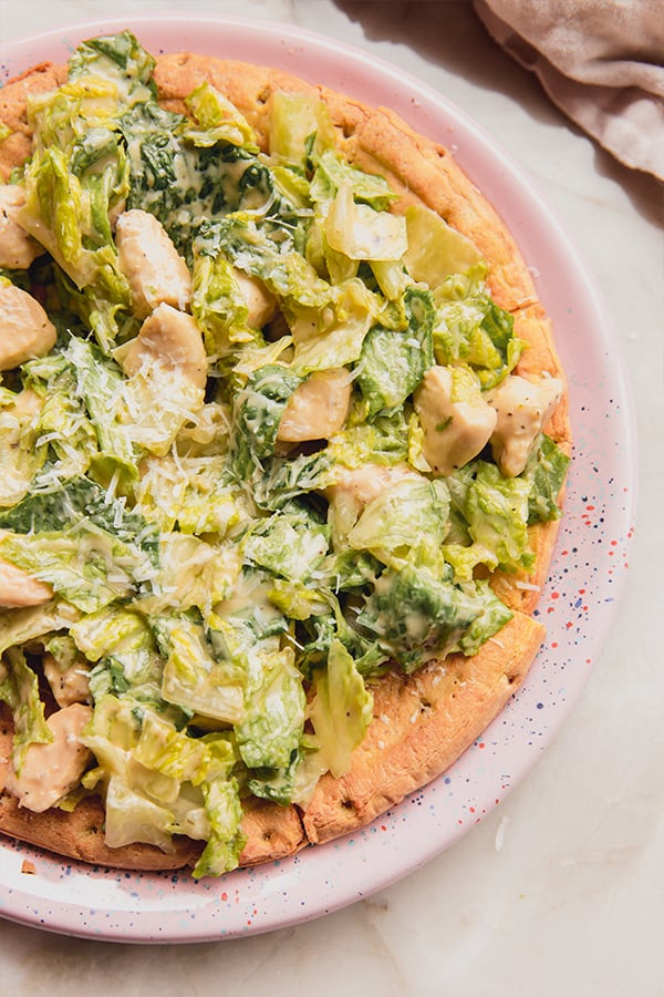 A plate with chicken caesar pizza on top of it.