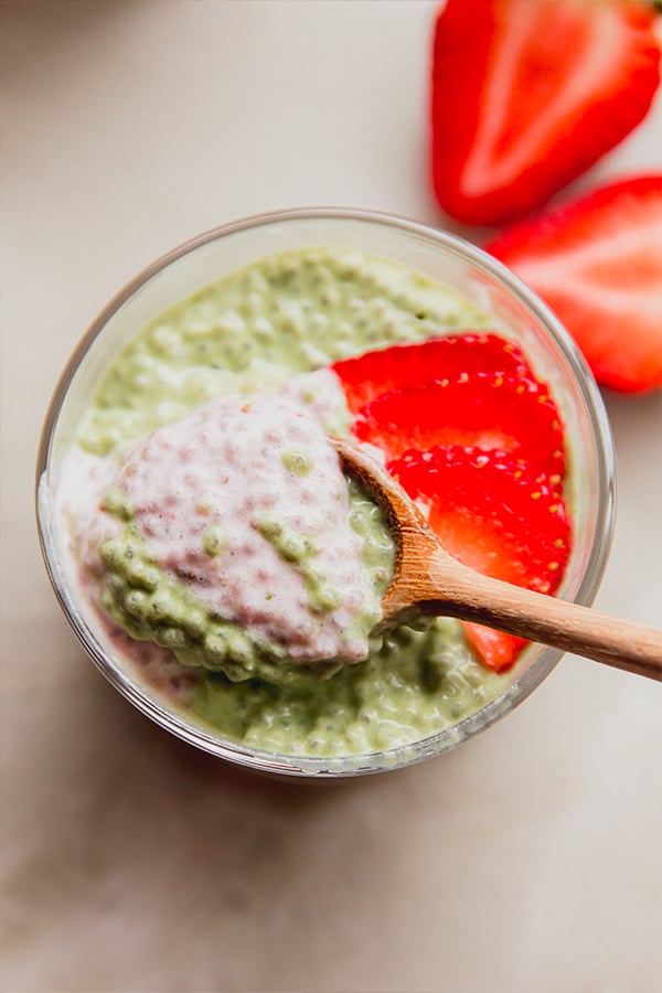 A cup of strawberry matcha chia pudding with a spoon taking a spoonful out of it.