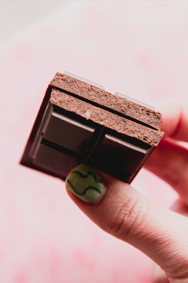 A homemade coconut milk chocolate bar broken in half and being held in a hand.