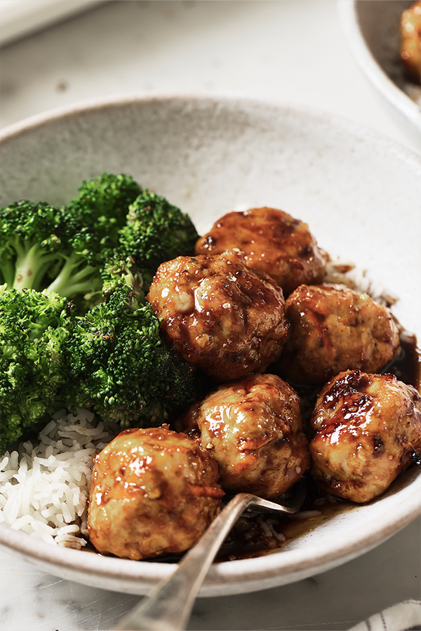 A bowl of honey garlic meatballs with broccoli and rice ready to be eaten.