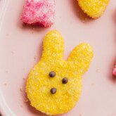A yellow easter bunny shaped marshmallow peep on a pink plate.