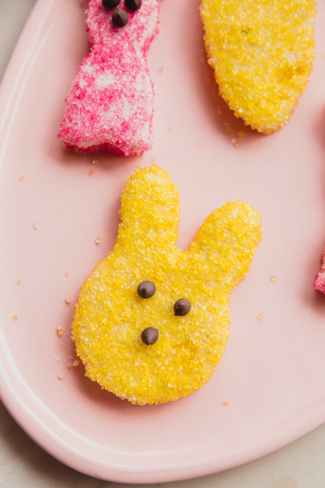 A yellow easter bunny shaped marshmallow peep on a pink plate.