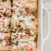 Chicken alfredo lasagna roll ups in a white baking dish, topped with chopped parsley and proscuitto.