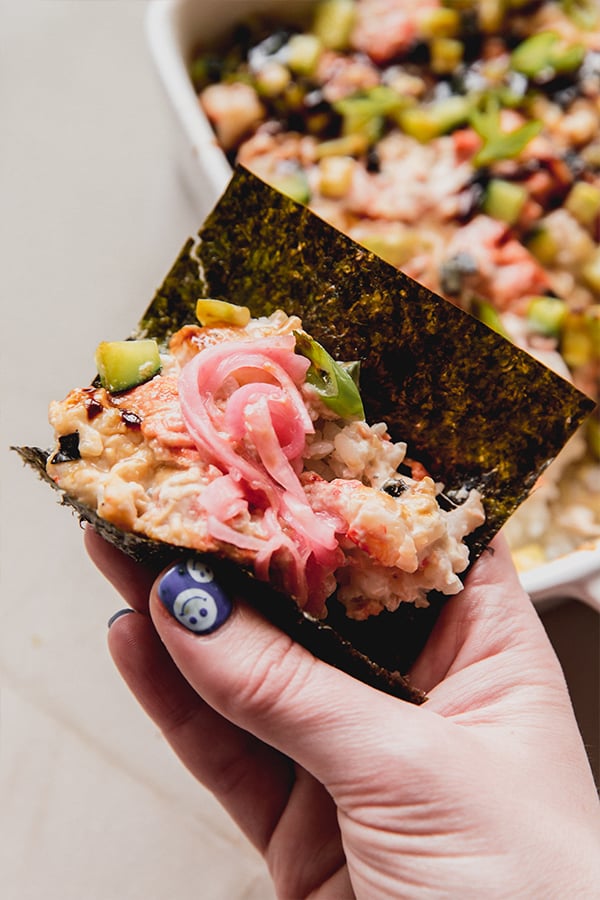A piece of seaweed wrapped around the mini sushi bake topped with pickled onions.