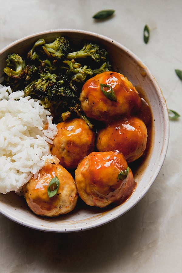 A bowl of sweet & sour chicken meatballs with broccoli and rice ready to be eaten.