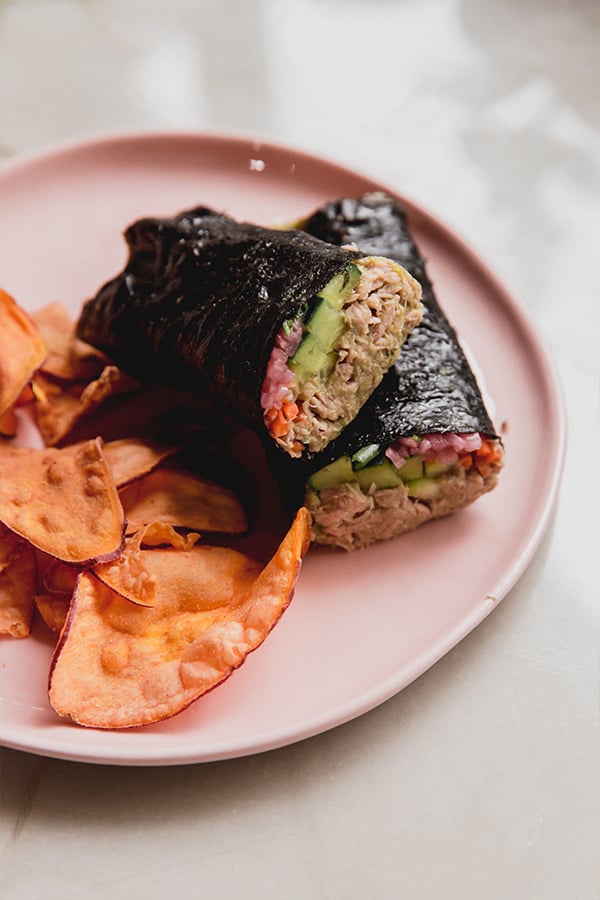 A plate with a tuna seaweed wrap cut in half with chips ready to be enjoyed.