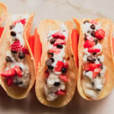 Cannoli tacos topped with strawberries and chocolate chips in a taco holder.