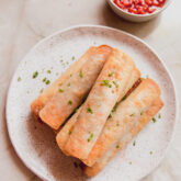 Veggie pizza rolls stacked on a plate topped with chopped parsley with sauce on the side in a bowl.