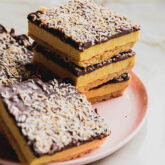 Lemon smores bars topped with toasted coconut, stacked on a pink plate.