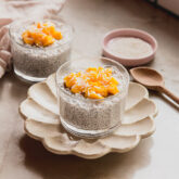 Mango sticky rice chia pudding topped with diced mango and coconut, with another bowl in the background and a small wooden spoon.