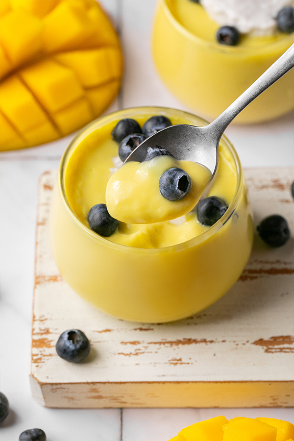 A cup of dairy-free mango pudding with a spoon taking a bite out.