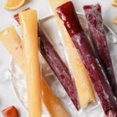 Fruit and veggie freezer pops stacked on top of eachother on a plate with ice and sliced fruit.