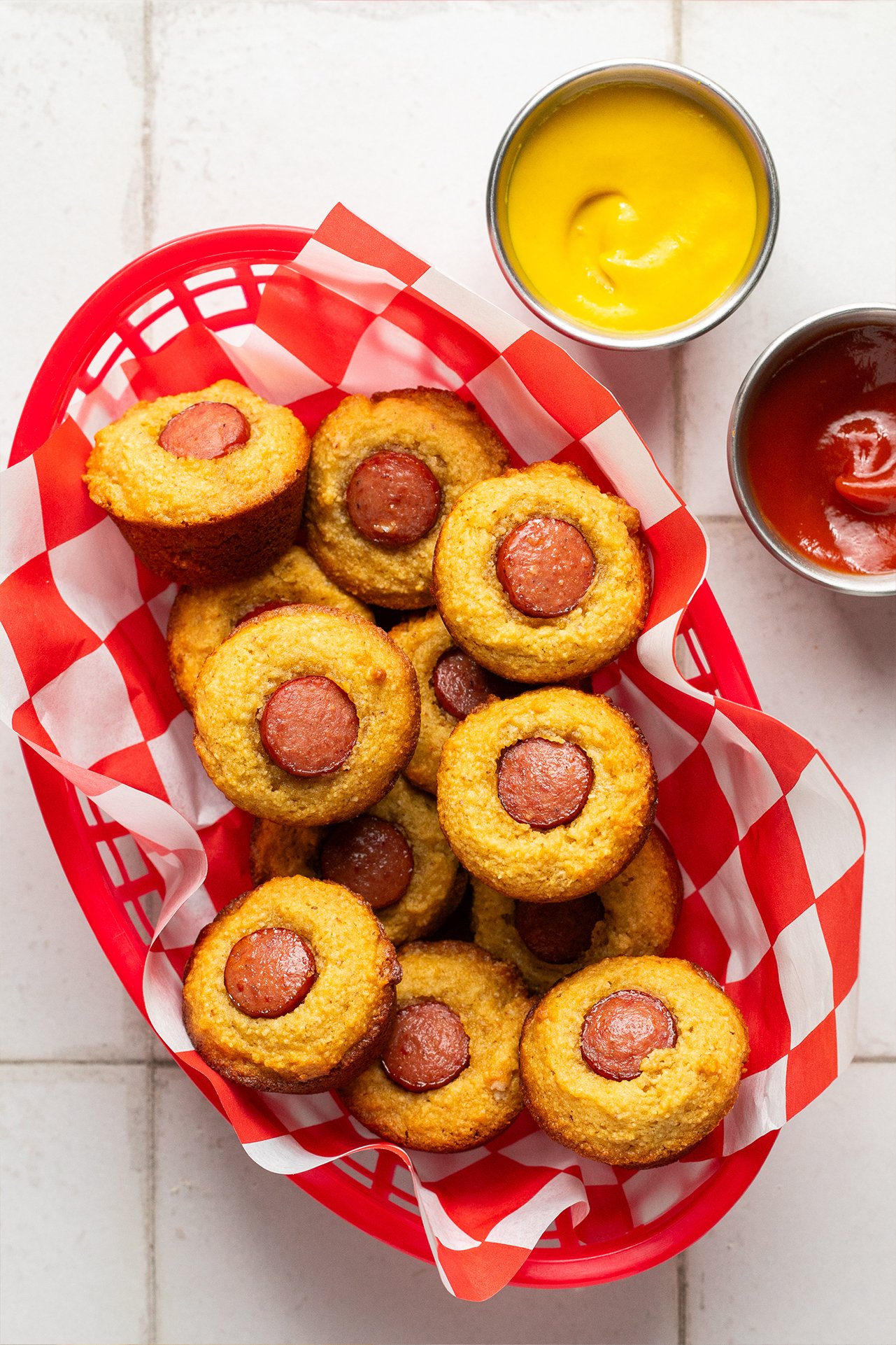 Corn dog muffins in a basket with mustard and ketchup.