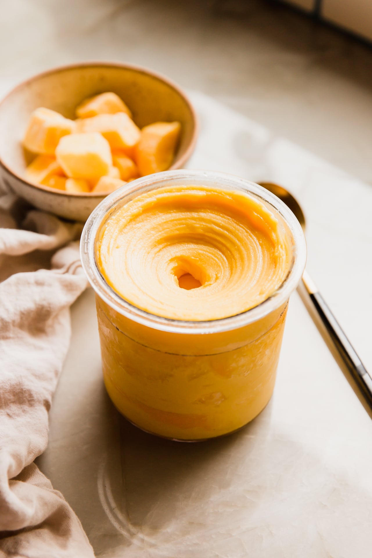 Mango ninja creami sorbet in a ninja creami container, with frozen mango in a bowl in the background.