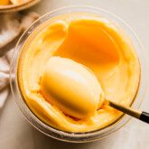 Mango ninja creami sorbet in a ninja creami container being scooped with a spoon.