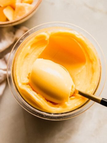 Mango ninja creami sorbet in a ninja creami container being scooped with a spoon.