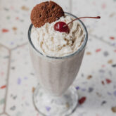 Ninja creami milkshake topped with whipped cream, a cookie and a cherry.