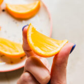 One orange jello slice being held with two fingers.