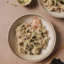 Avocado tuna rice bowl in a beige bowl and topped with pickled ginger on the side.