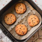 Air fryer chocolate chip cookies, fully cooked on parchment paper in the air fryer basket.