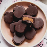 Almond butter cups shapes like pumpkins on a pink plate, with a bite taken from one.