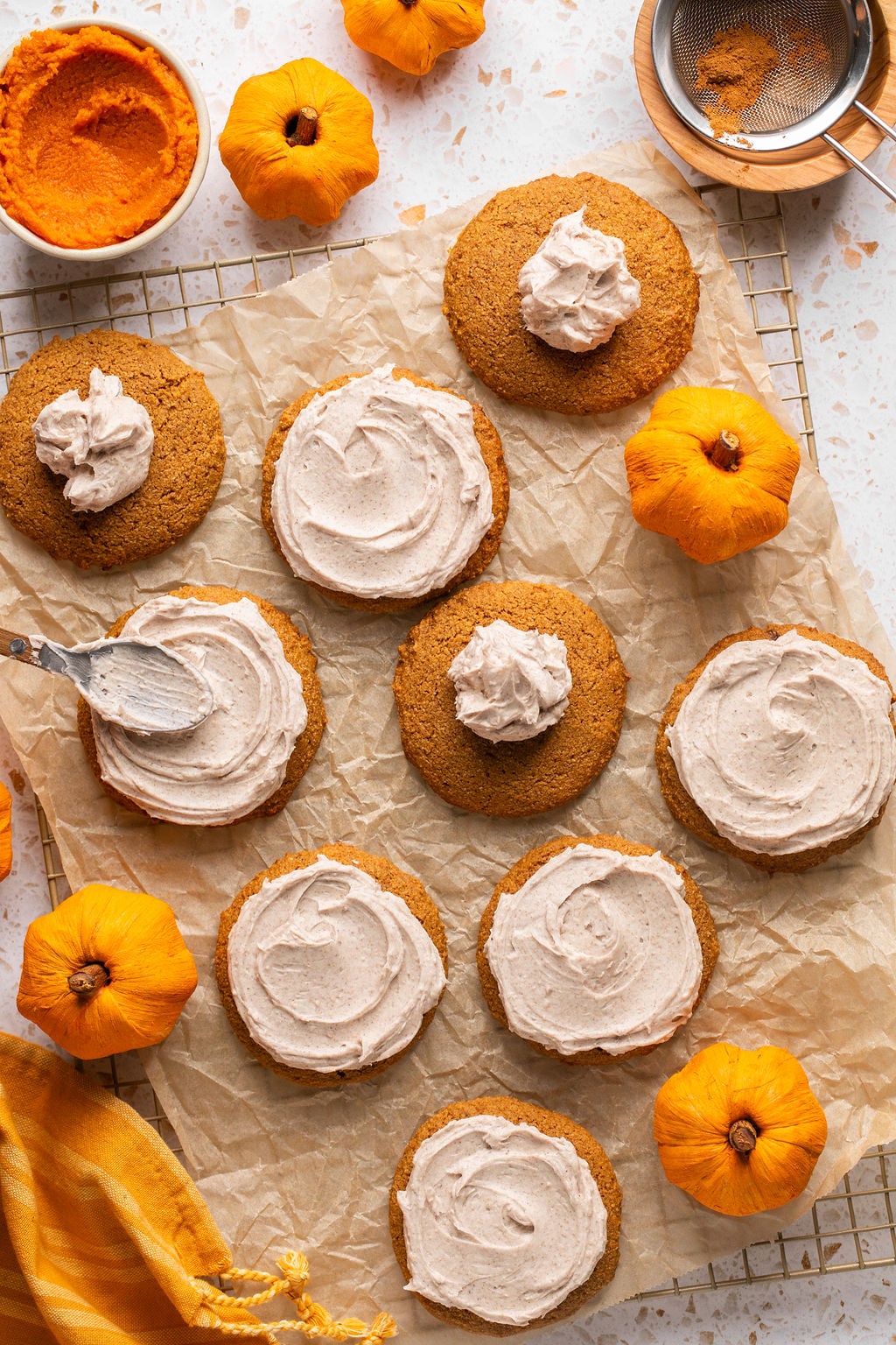 Pumpkin cookies on a wire rack with icing being spread on.