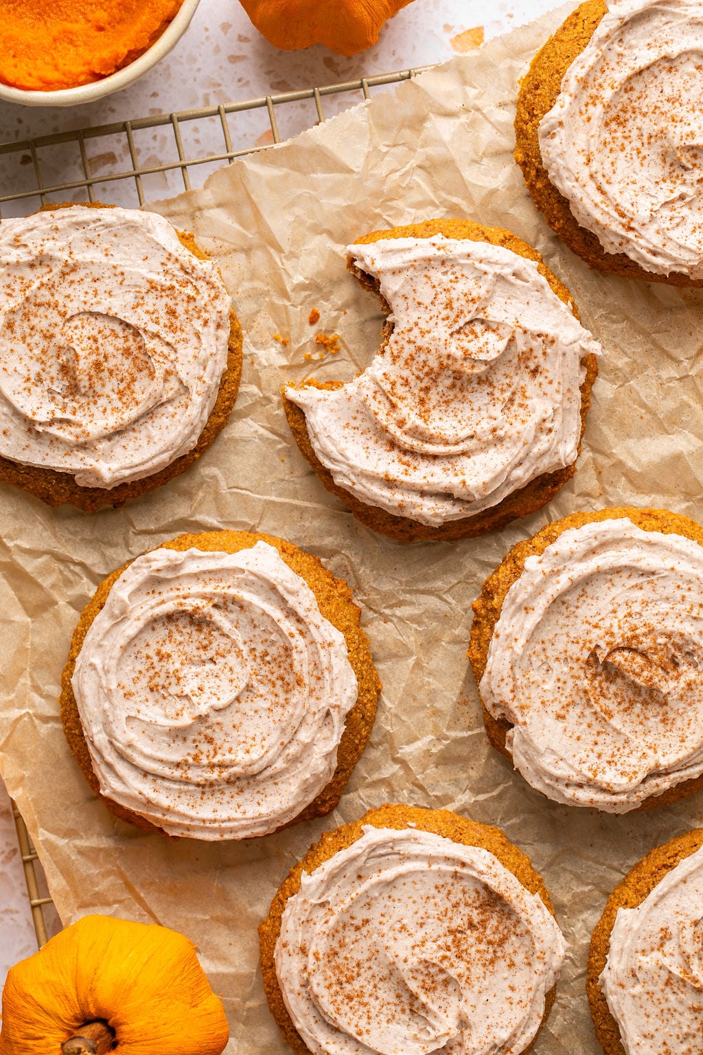 A beautifully arranged stack of gluten-free pumpkin cookies, generously topped with creamy latte frosting and a light sprinkle of pumpkin pie spice, resting on a wire rack with parchment paper.