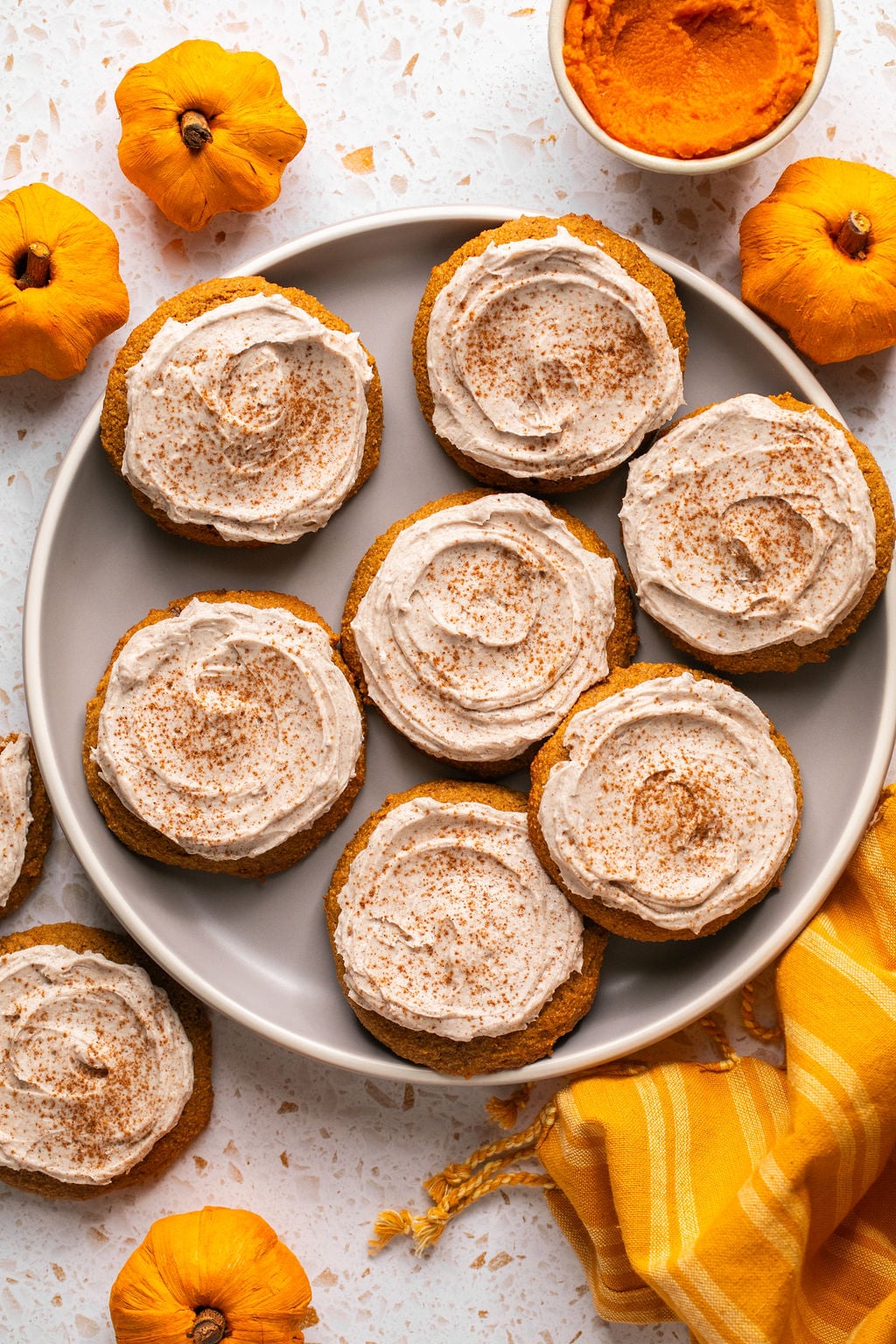 Pumpkin cookies topped with frosting on a large plate.