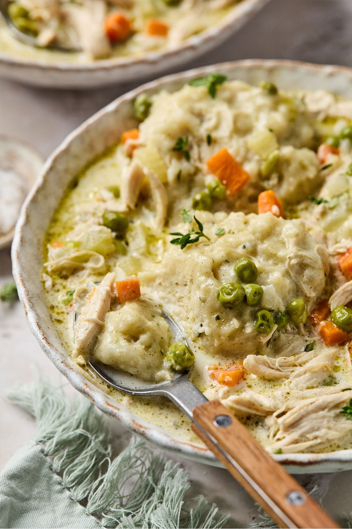 chicken and dumplings soup in a bowl  with a spoon cutting the dumpling in half. 