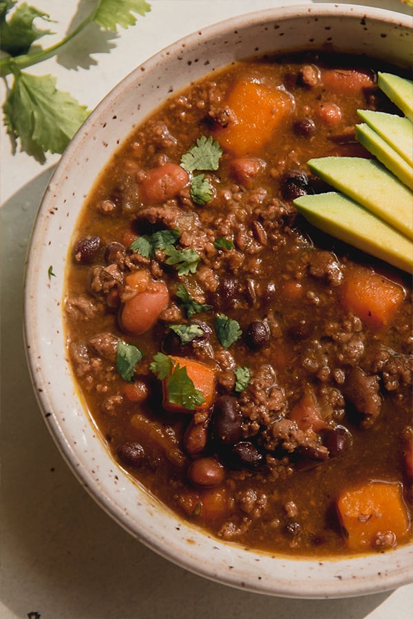 Nightshade free chili in a bowl topped with cilantro and fresh avocado. 