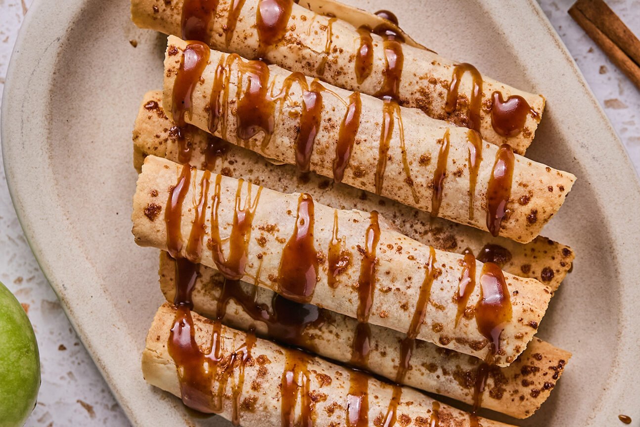 Apple pie roll ups on a platter drizzled with caramel.