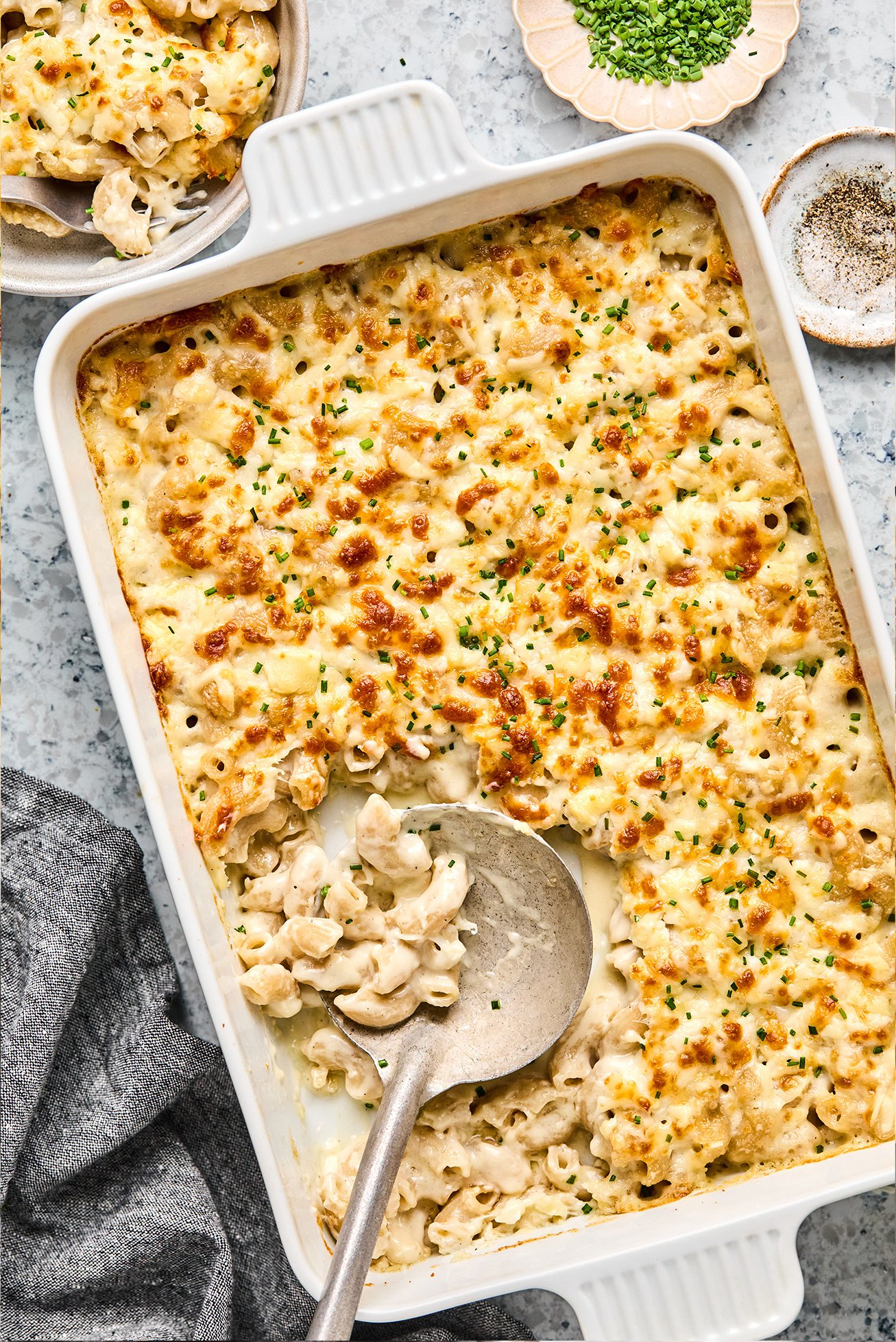 Goat cheese mac and cheese in a baking dish with a bowl of mac and cheese on the side.