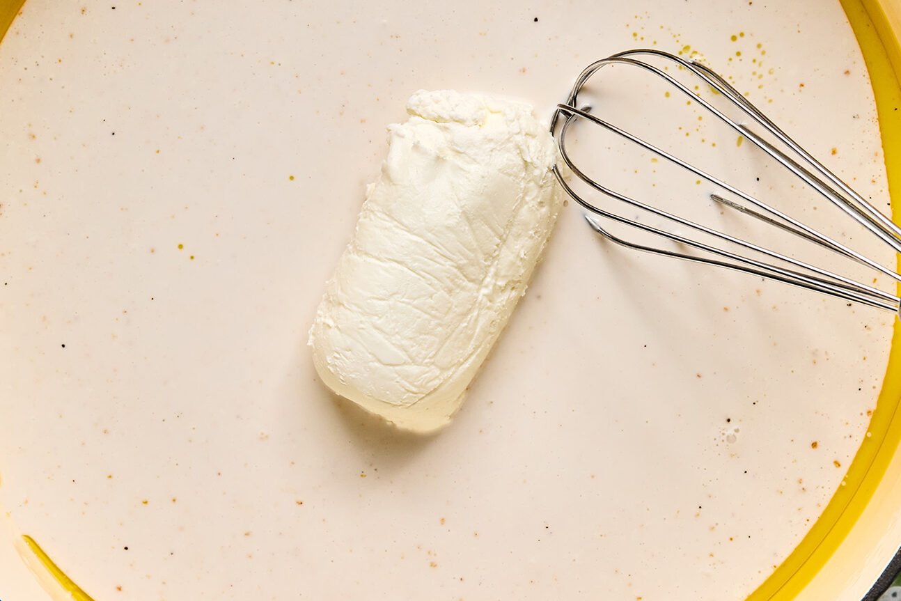 Goat cheese being mixed into a coconut milk mixture with a whisk.