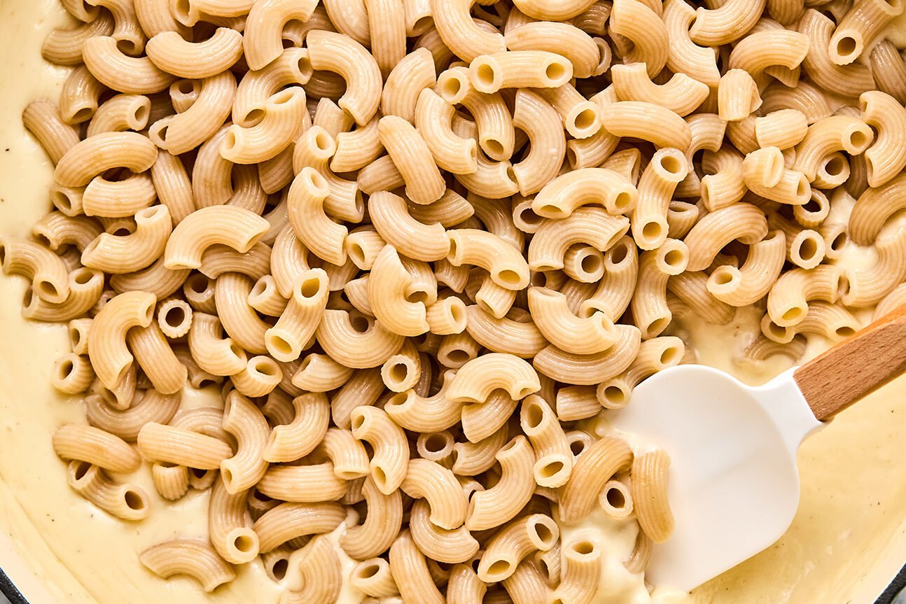 A bowl with goat cheese sauce under cooked pasta.